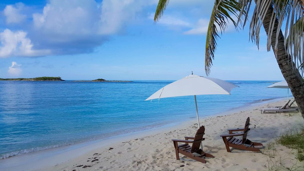 A quiet Bahamian beach with palm trees, umbrellas, and turquoise water